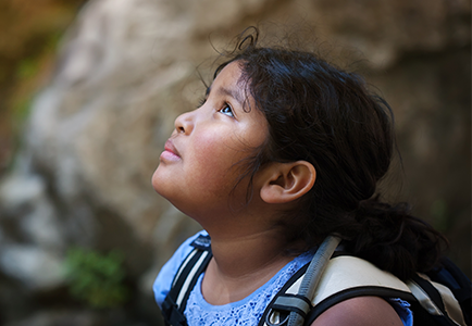 Young girl with backpack looks up towards the sky